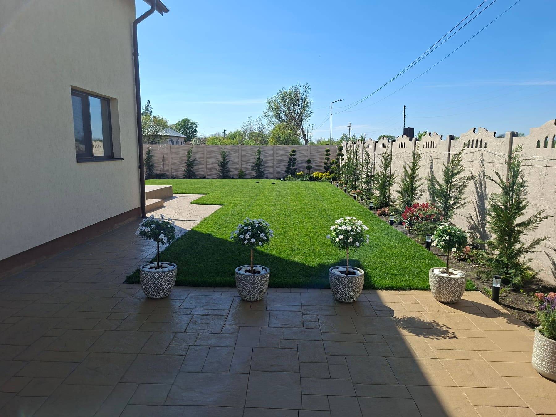 Grădină amenajată de Floval Garden, cu gazon, conifere și ghivece cu flori